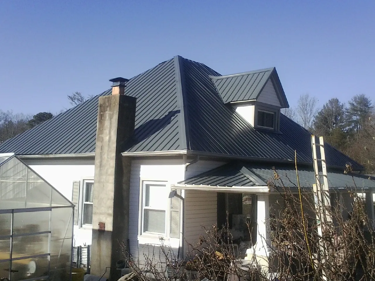 Dark blue standing seam metal roof on a white farmhouse with dormer — Slate & Tile Roof Repair by Roofing Brothers in White Castle