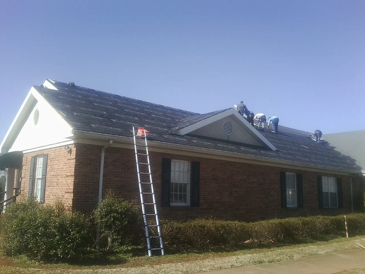Crew tearing shingles off a brick ranch roof with a ladder set — Metal Roof Repair work by our crew in White Castle