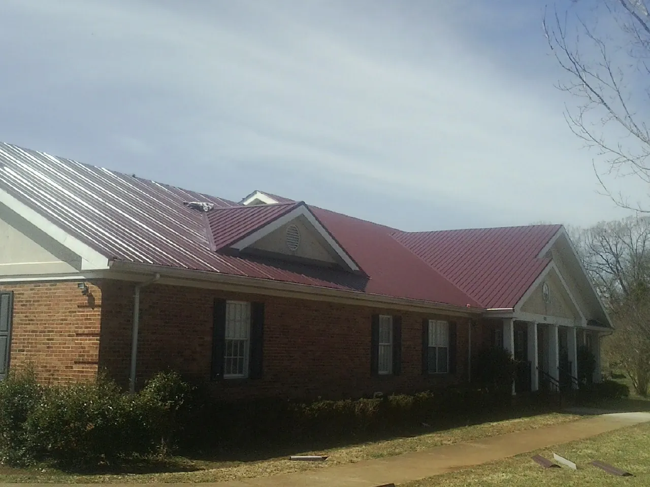 Red metal roof with gabled entries on a long brick building, from a Hail Damage Roof Repair job in White Castle