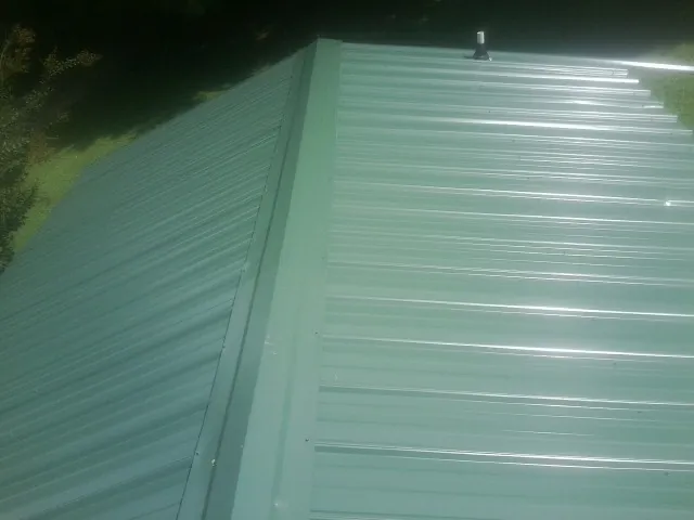 New green metal panels meeting at the ridge of a roof — Flat Roof Repair work by our crew in White Castle