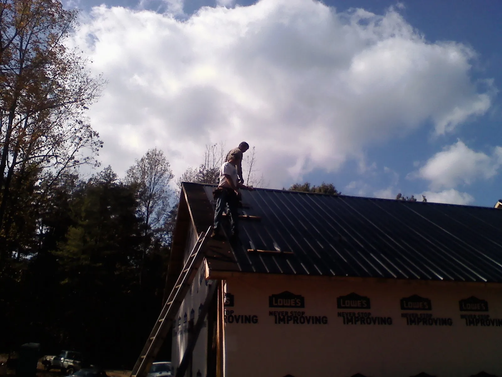 Roofer fastening dark metal panels high against a cloudy sky, from a Roof Inspection job in White Castle